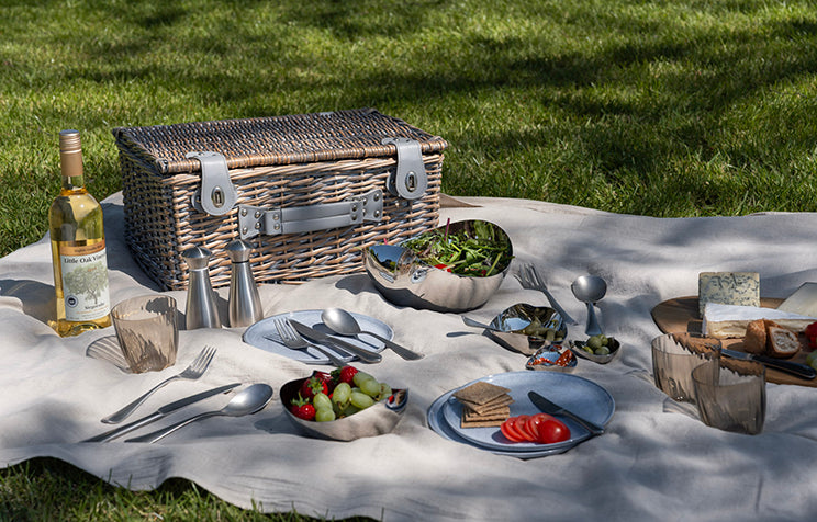 Picnic setup with food, drinks, Robert Welch cutlery, salt and pepper mills, and serving bowls.
