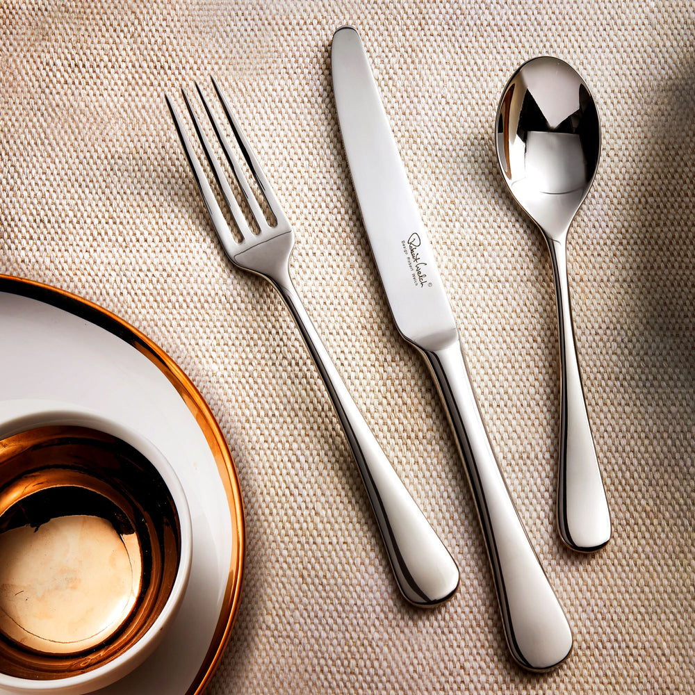 Silver fork, knife, and spoon set on a textured beige surface with a candle in the corner.